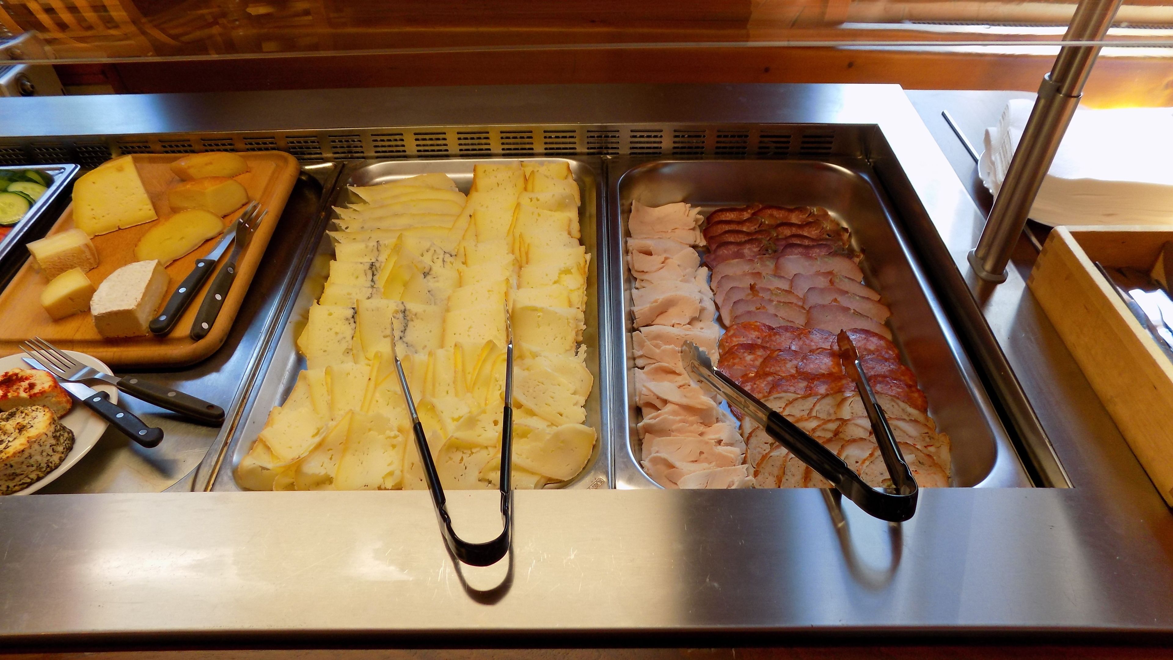 Un bufé con diferentes opciones de comida, incluyendo queso, papas y jamón.