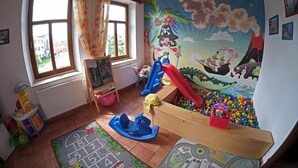 Un cuarto de juegos infantil con un tobogán, piscina de pelotas y alfombras educativas.
