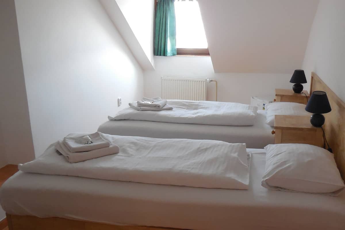 Una habitación con dos camas, cabeceros de madera, una mesita de noche con lámpara y un ventanal con cortinas.