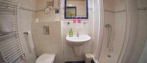 A bathroom with a white toilet, a sink with a mirror above it, a shower area, and a blue-tiled floor.