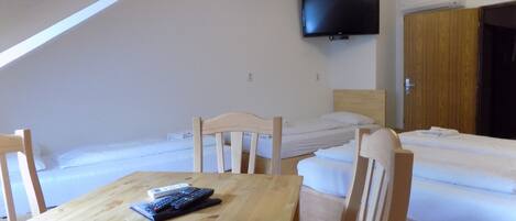 Ein Zimmer mit Holztisch, zwei Betten, einem an der Wand befestigten Fernseher und einem Schrank.