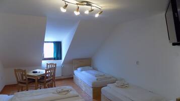 A small, well-lit room with a sloped ceiling, a desk with a chair, and two single beds.