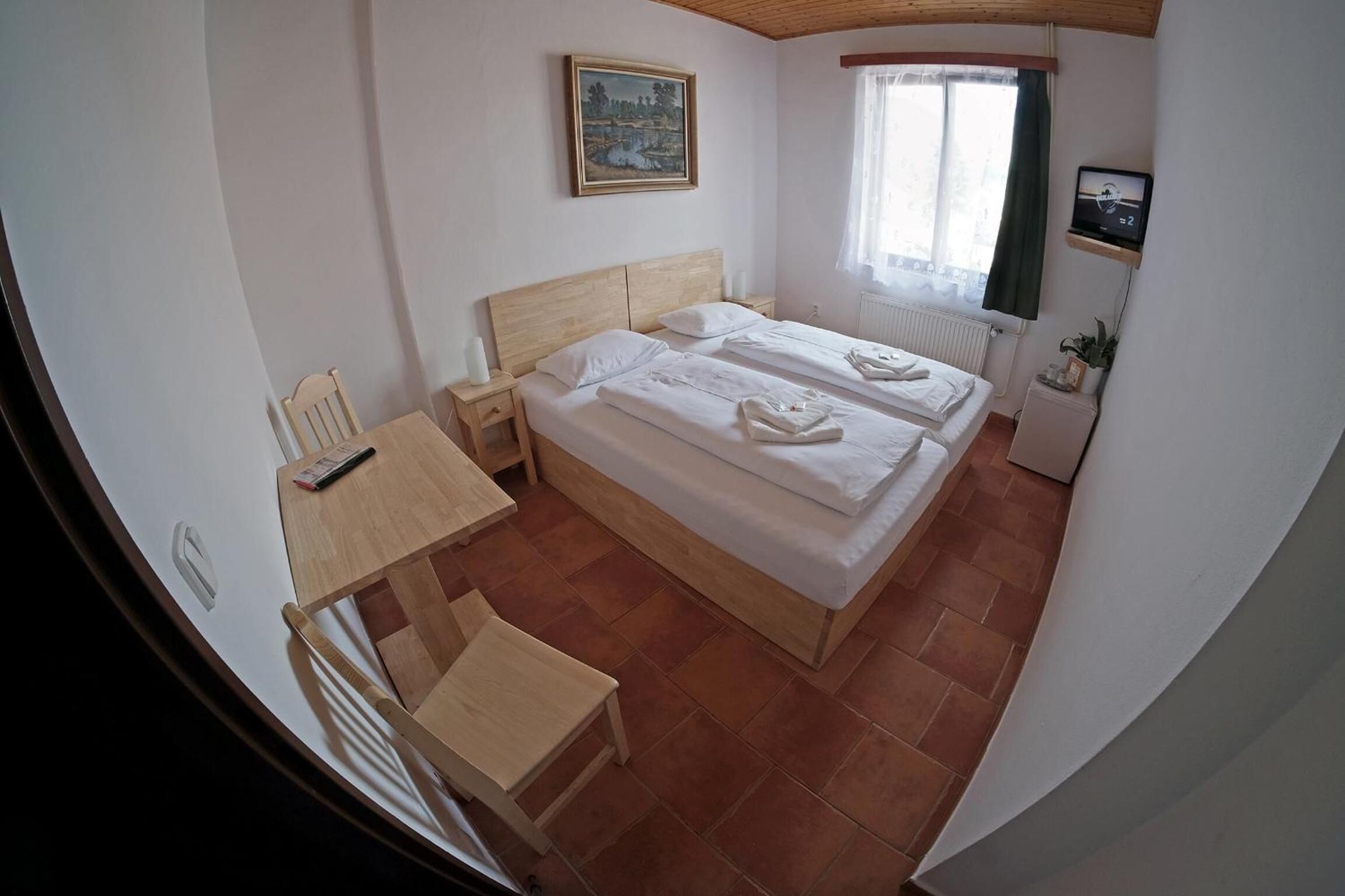 A bedroom with two beds, a wooden desk, a chair, a painting on the wall, a TV, and a window with curtains.