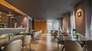 A modern restaurant with multiple dining tables and chairs, a bar area with shelves of bottles, and a decorative wall with a geometric pattern. - Burgus Tribute & Design Hotel (Braga)