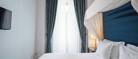 A hotel room with a large bed, a TV mounted on the wall, and a window with curtains.
