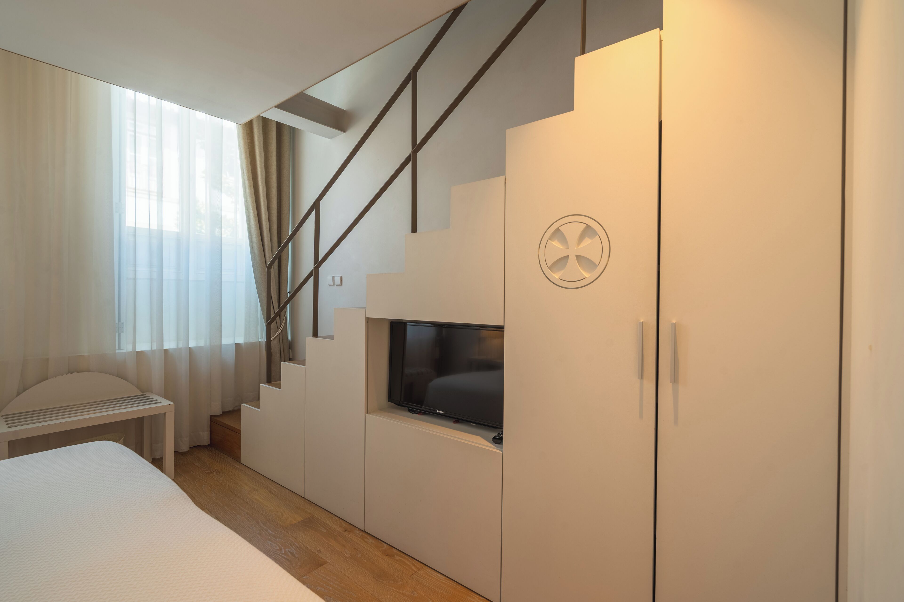 Quarto moderno com cama, televisão na parede, escada e guarda-roupa.