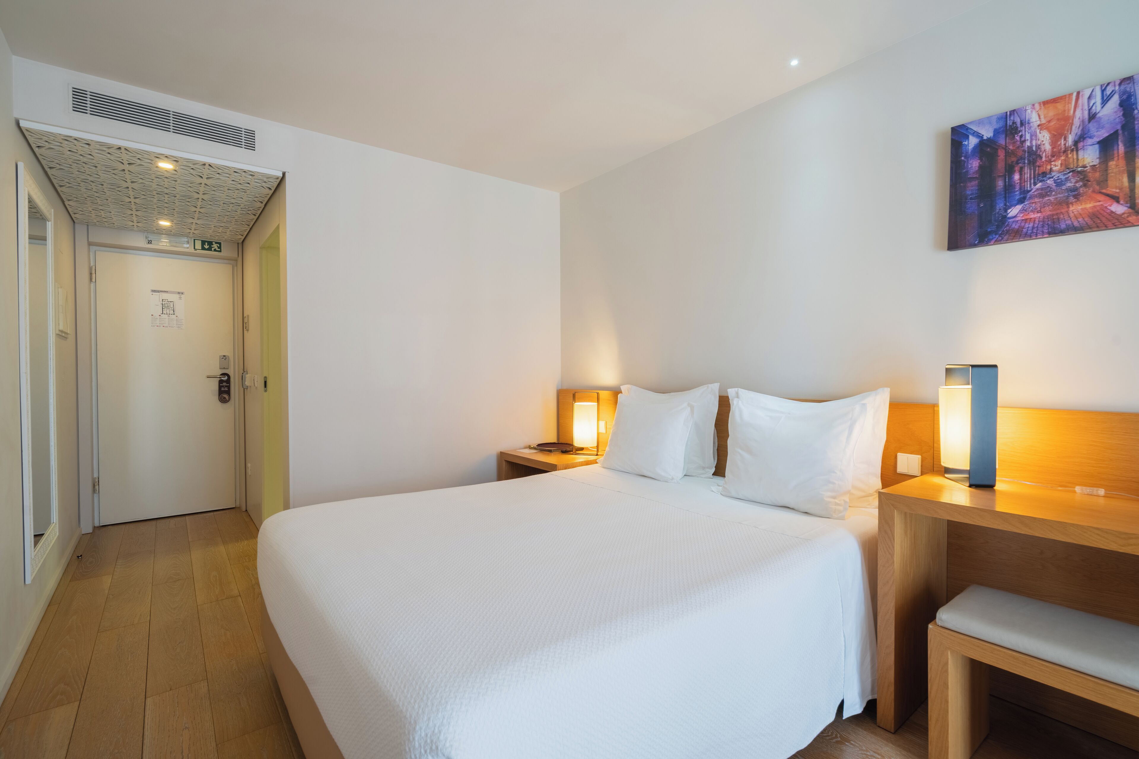 Une chambre d’hôtel avec un grand lit, des tables de chevet avec des lampes, un banc en bois et un tableau au mur.