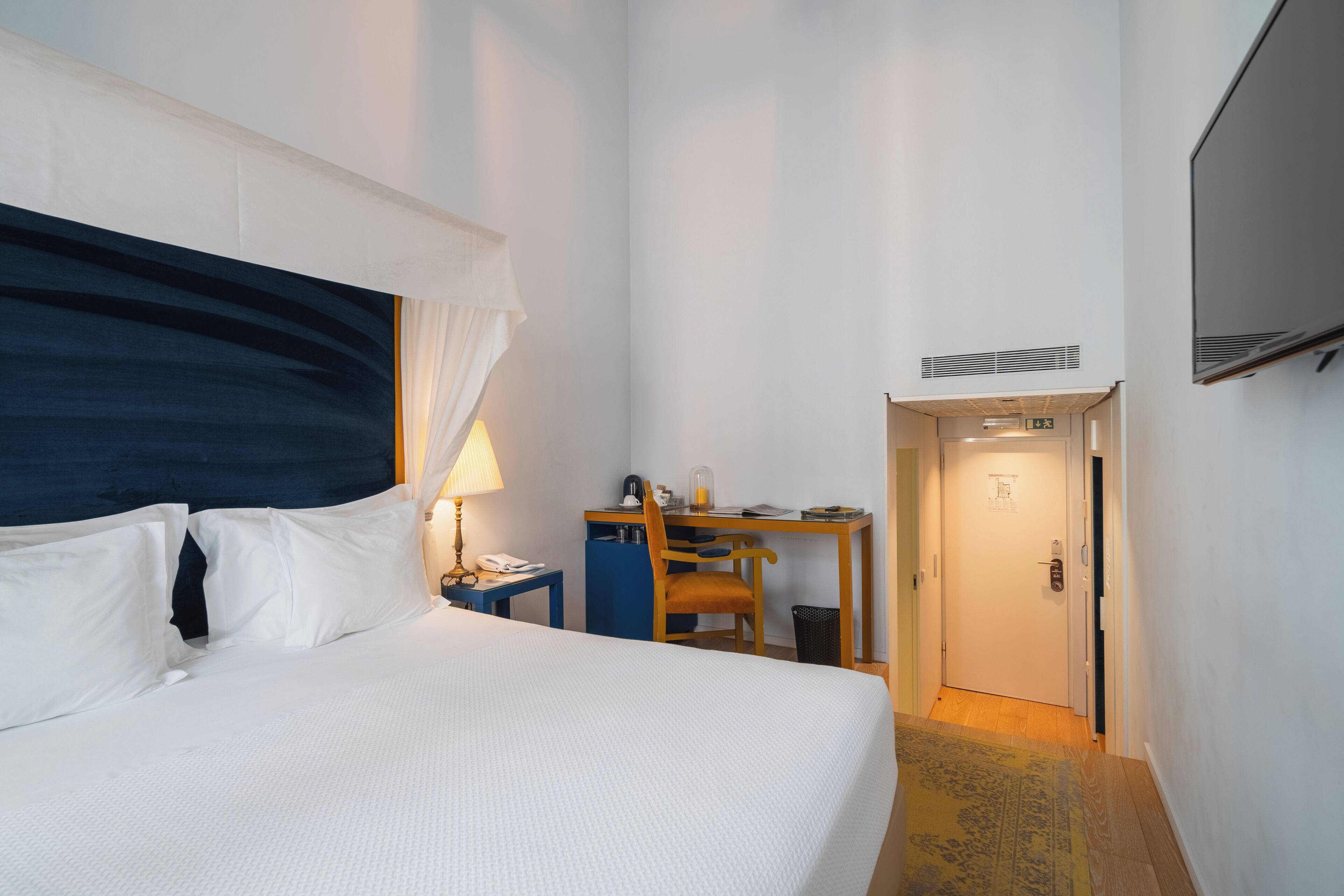 Ett hotellrum med en säng, ett skrivbord, en stol, en lampa och en tv.