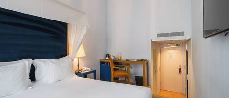 Ett hotellrum med en säng, ett skrivbord, en stol, en lampa och en tv.