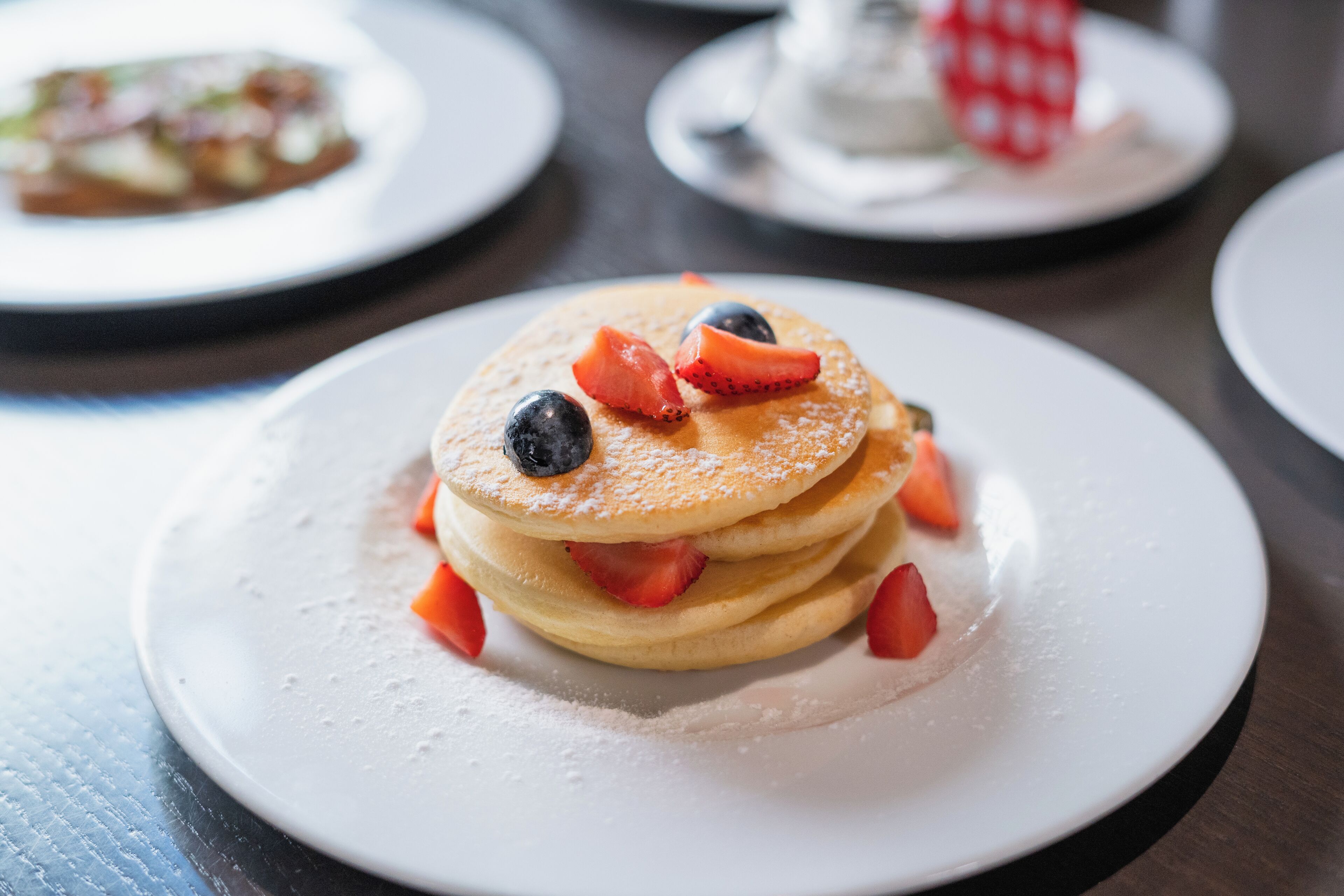 A stack of pancakes with strawberries and blueberries on a white plate.