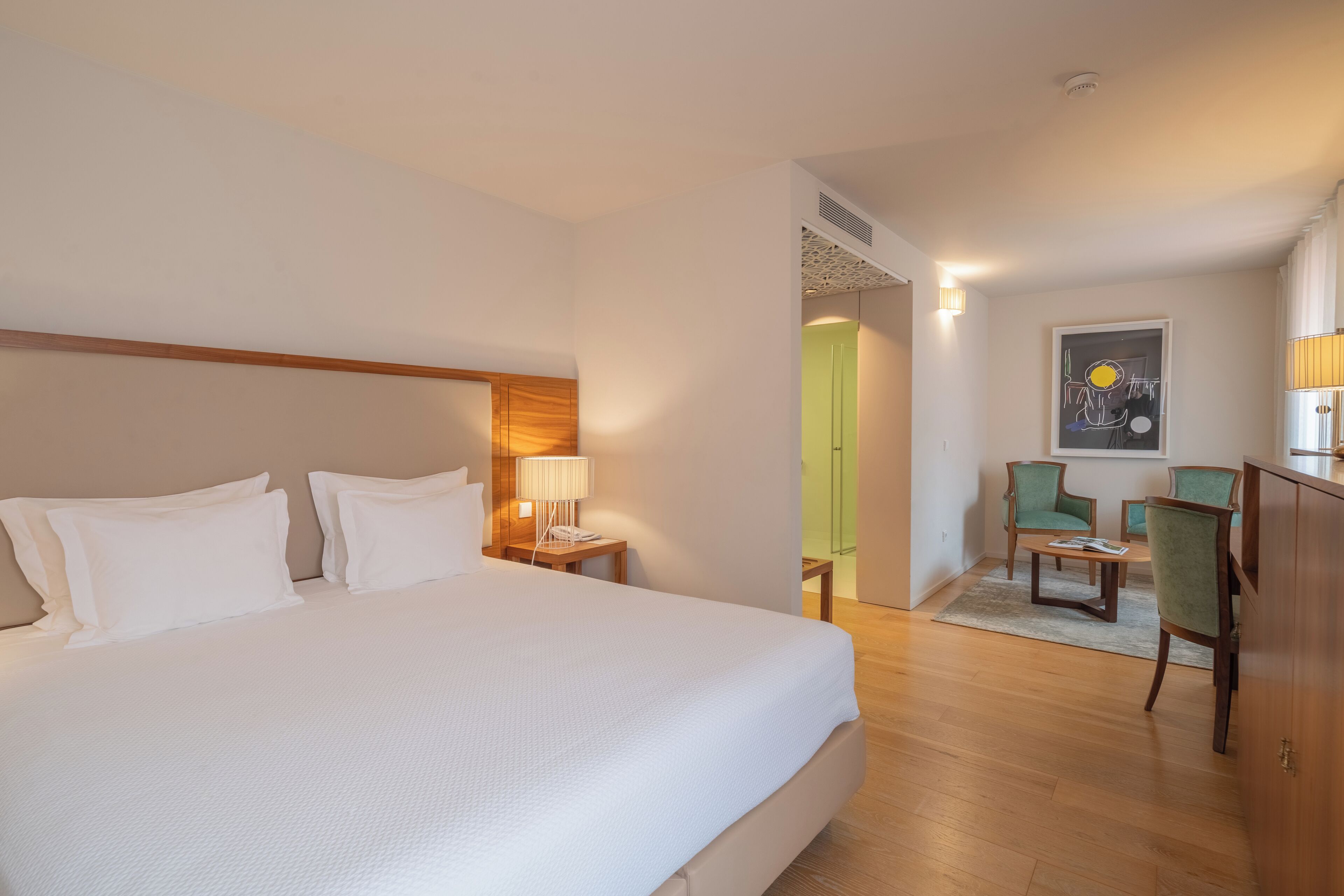 A hotel room with a large bed, a desk with two chairs, a lamp, and a painting on the wall.
