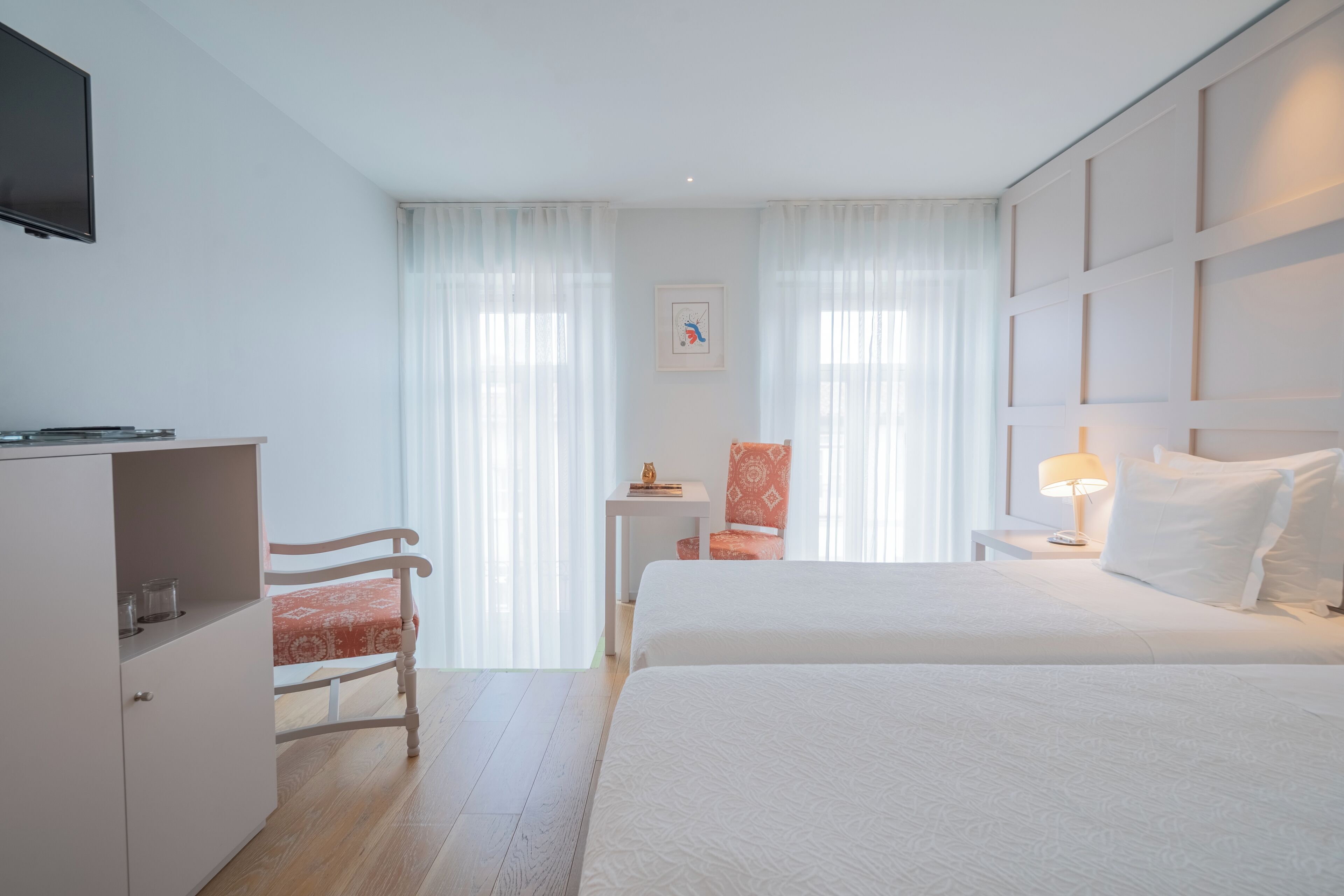 Hotellihuone, jossa on sänky, työp öytä, tuoli, televisio ja ikkuna, jossa on verhot.