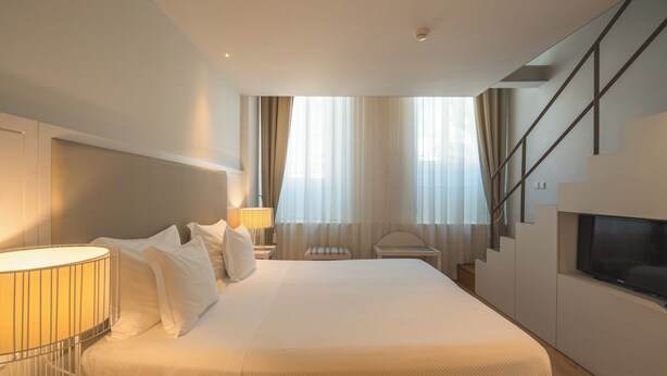 A modern hotel room with a large bed, a TV, a desk, and a staircase. - Burgus Tribute & Design Hotel (Braga)