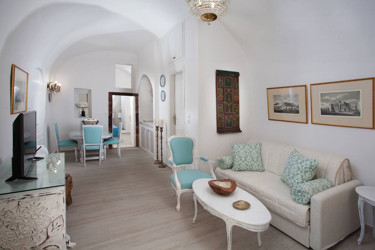 Amplia sala de estar con sofá, sillones, una mesa de centro y televisor. En el fondo, un comedor con mesa y sillas.