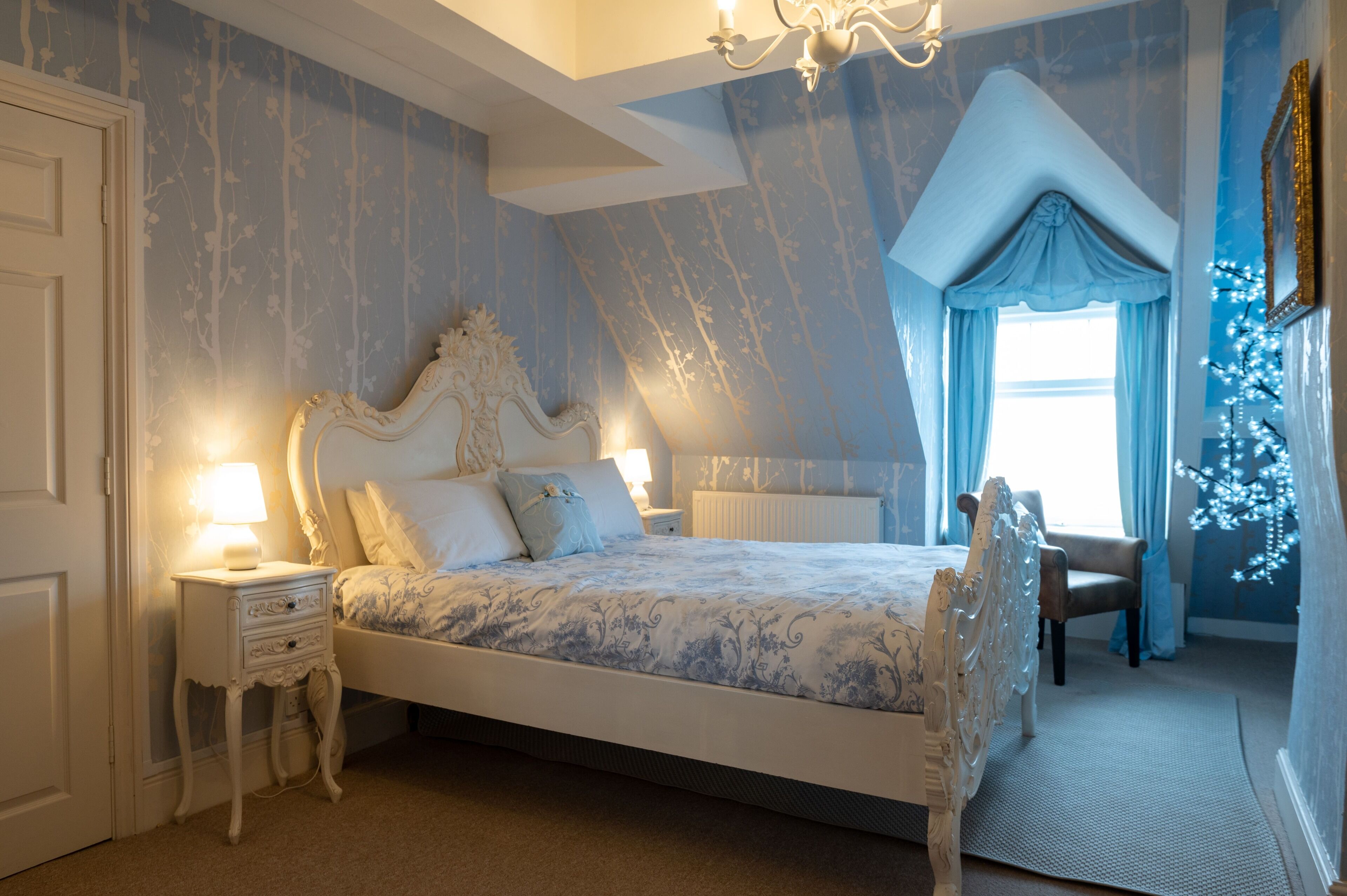 A bedroom with a large bed, a nightstand, a chair, and a window with curtains.