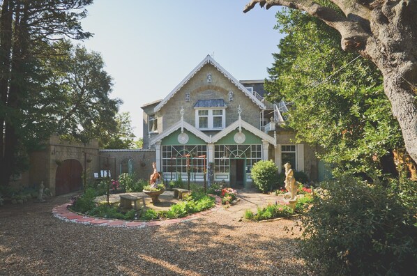 Un bâtiment traditionnel doté d’une façade en pierre, d’un toit végétalisé et d’un jardin agrémenté de statues et d’une fontaine.