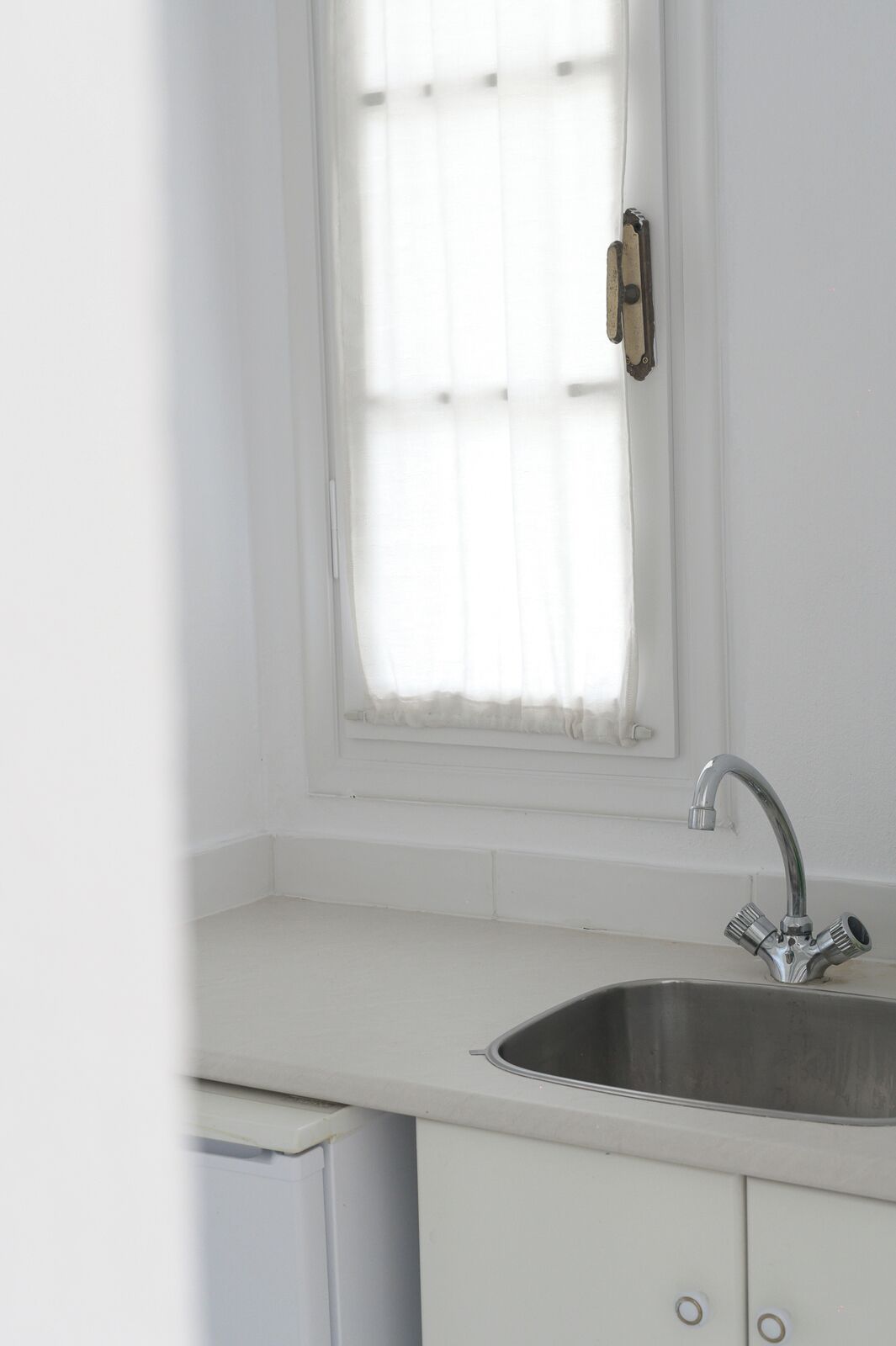 A kitchen with a white countertop, a stainless steel sink, and a window with a white blind.