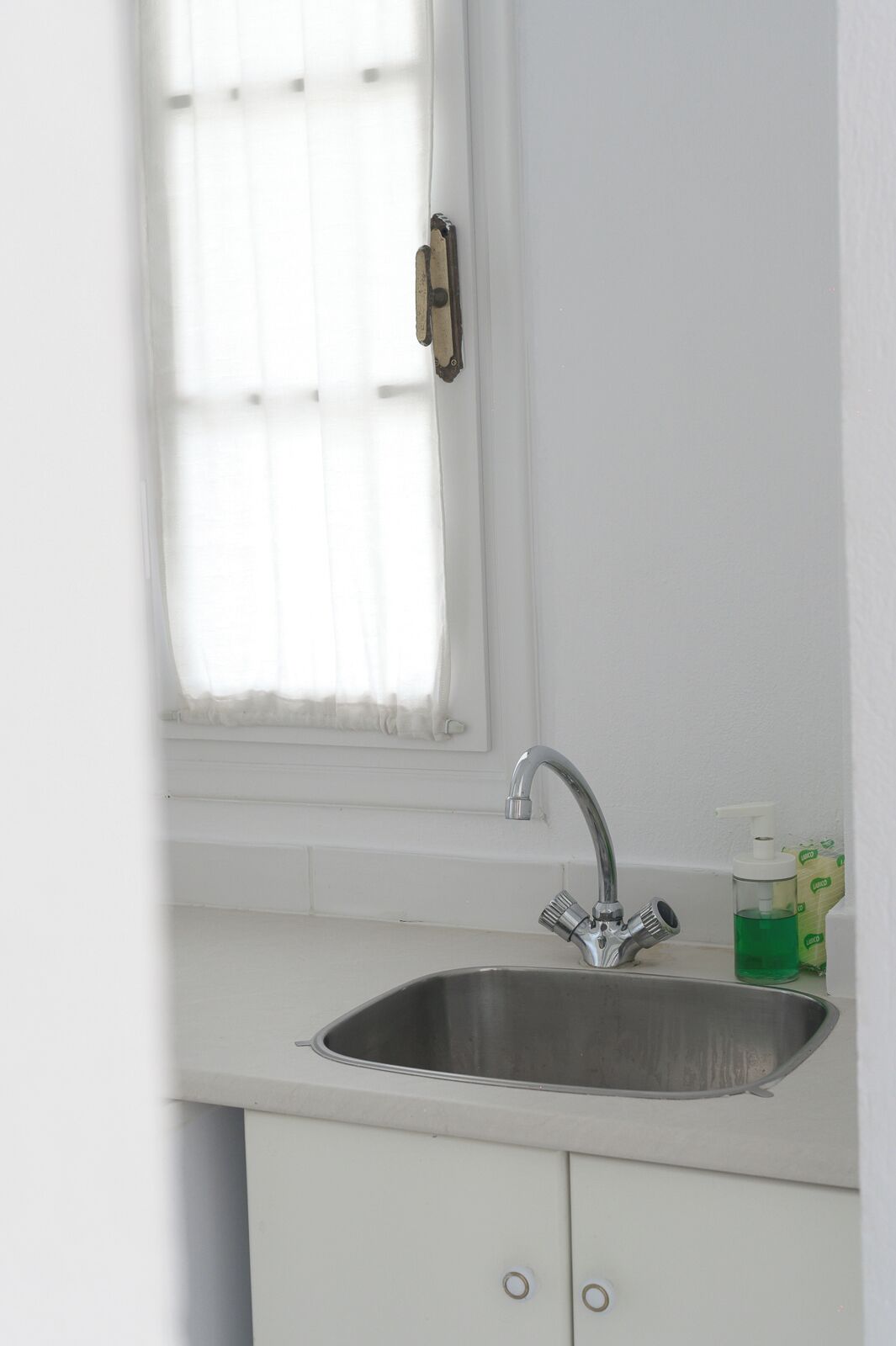 A kitchen with a stainless steel sink, a window with blinds, and a soap dispenser on the counter.