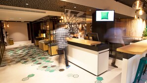 Een moderne hotel receptie met een digitaal scherm waarop de hotelnaam staat, een receptiebalie en een vloer met een patroon.
