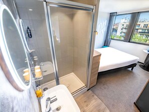 Ein modernes Badezimmer mit Dusche, Waschbecken und Toilette, ein Bett und ein Fenster mit Blick auf die Stadt.