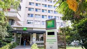 Een ingang van het ibis Styles hotel, met een bord waarop voorzieningen staan zoals een werkruimte, een kleine kitchenette en wifi.