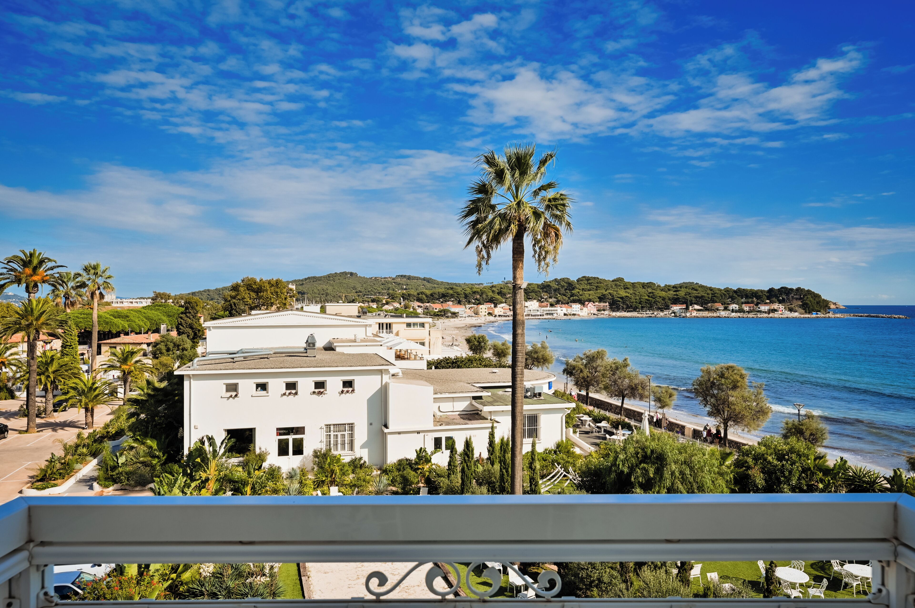 A coastal view with a white building, palm trees, and a clear blue sky.