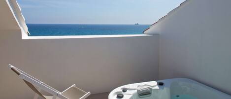 A balcony with a hot tub and a white chair.