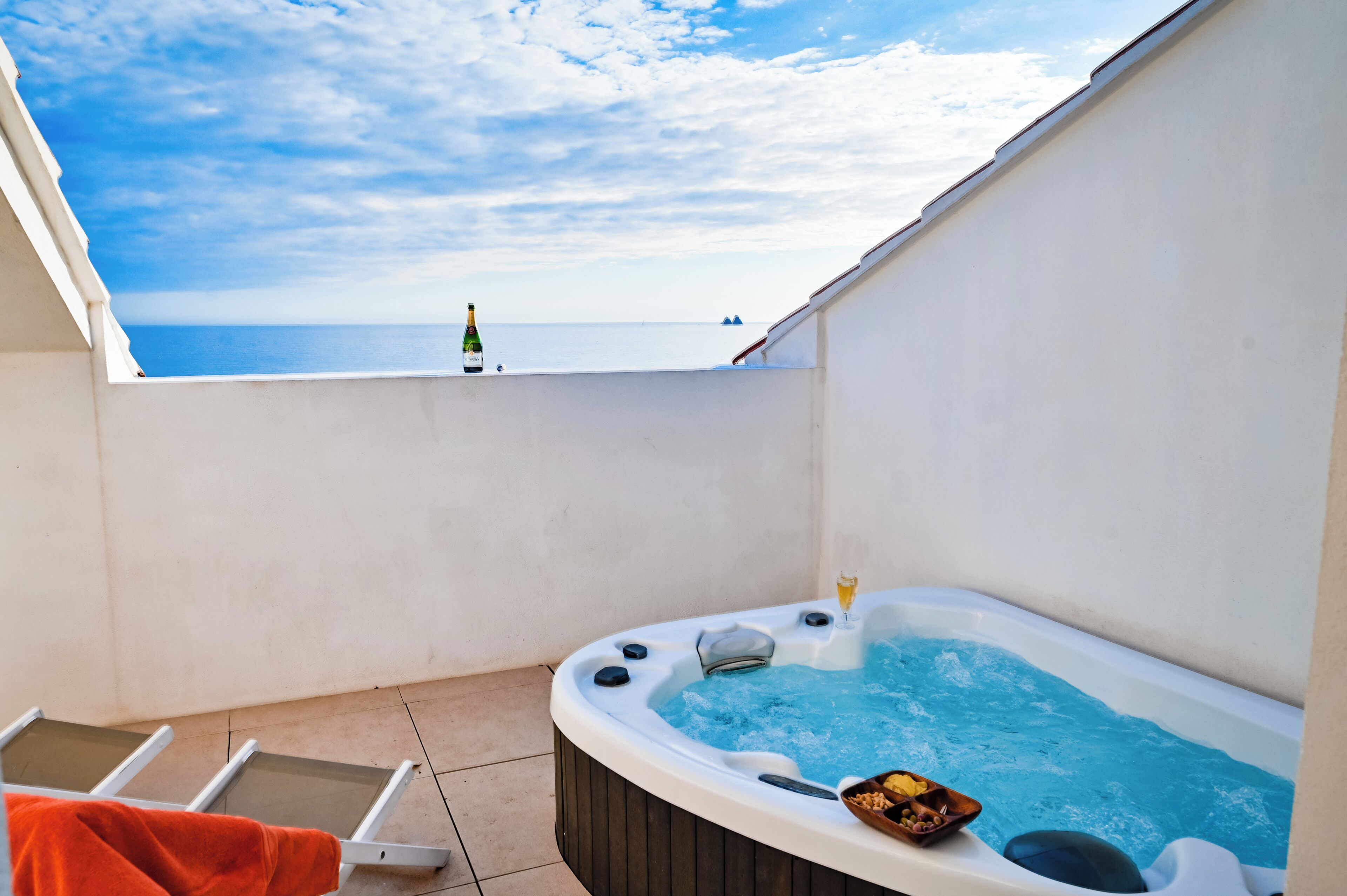Un jacuzzi con vista al mar, una botella y un bol de aperitivos.