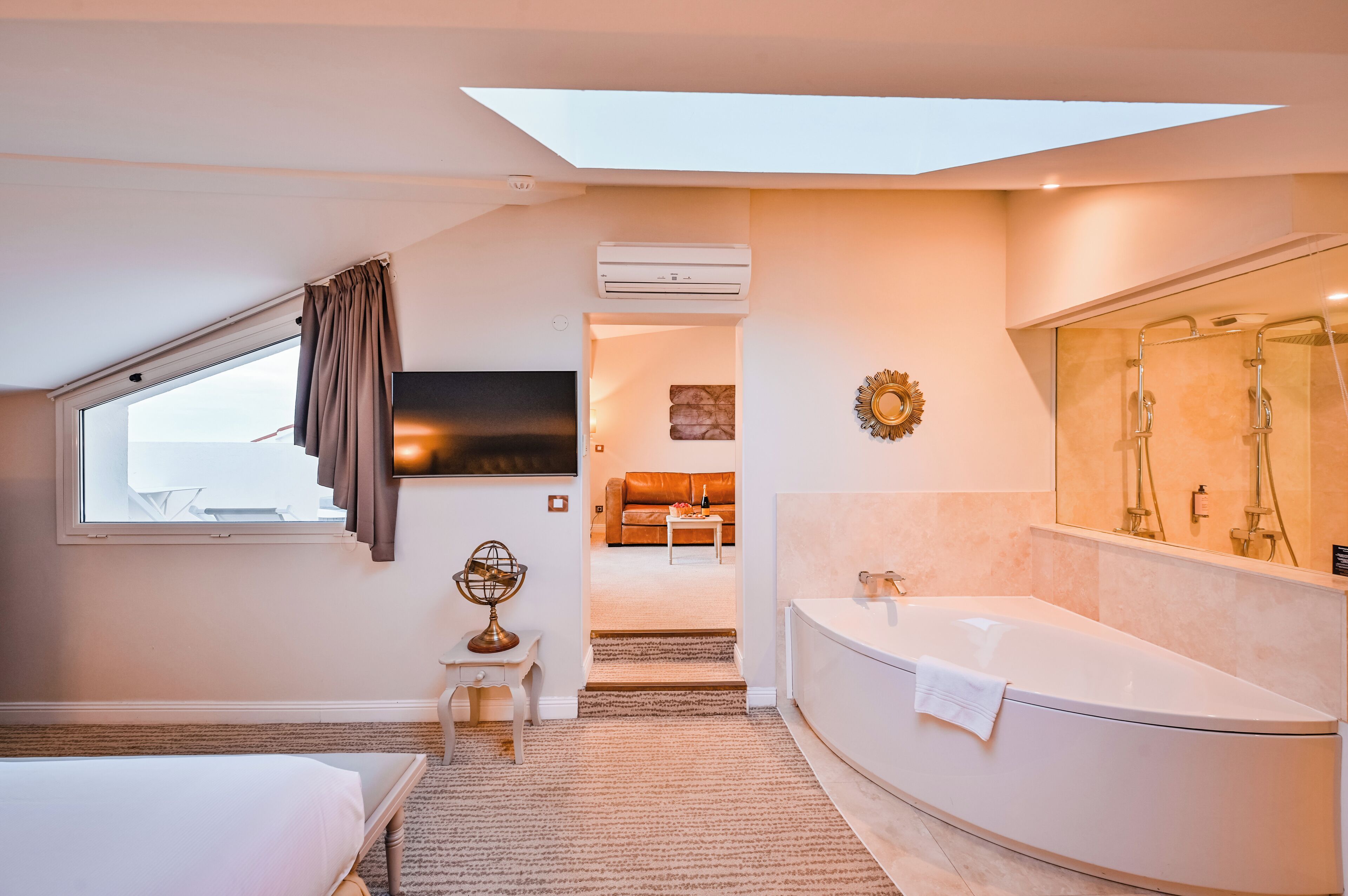 Une chambre d’hôtel moderne dotée d’une lucarne, d’une grande baignoire, d’un téléviseur et offrant une vue sur l’espace de vie.