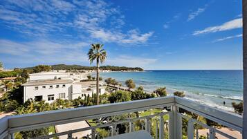 A balcony with a view of the sea, a palm tree, and a building with multiple windows.