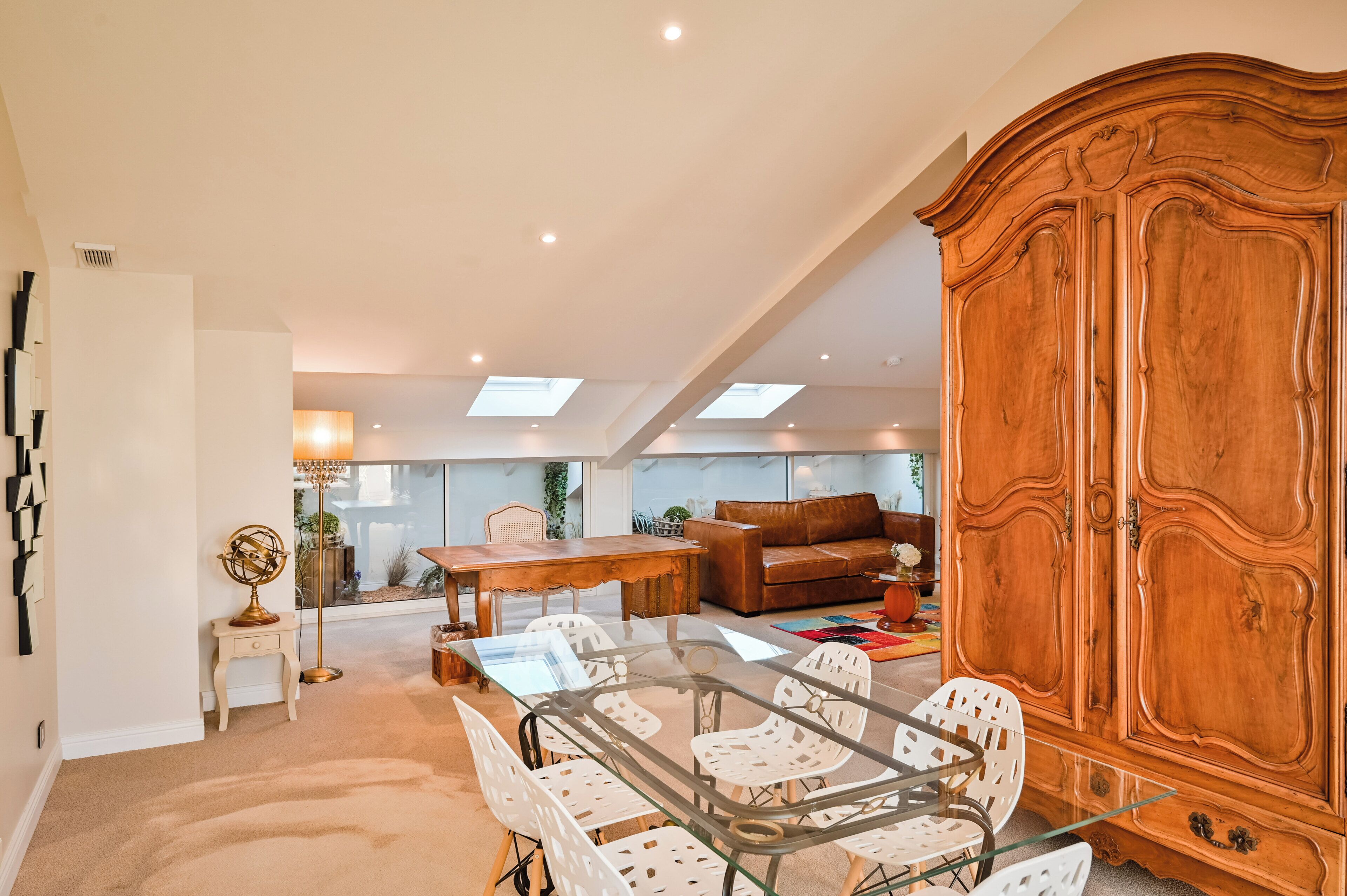 A spacious living area with a glass dining table, a brown leather sofa, and a large wooden cabinet.