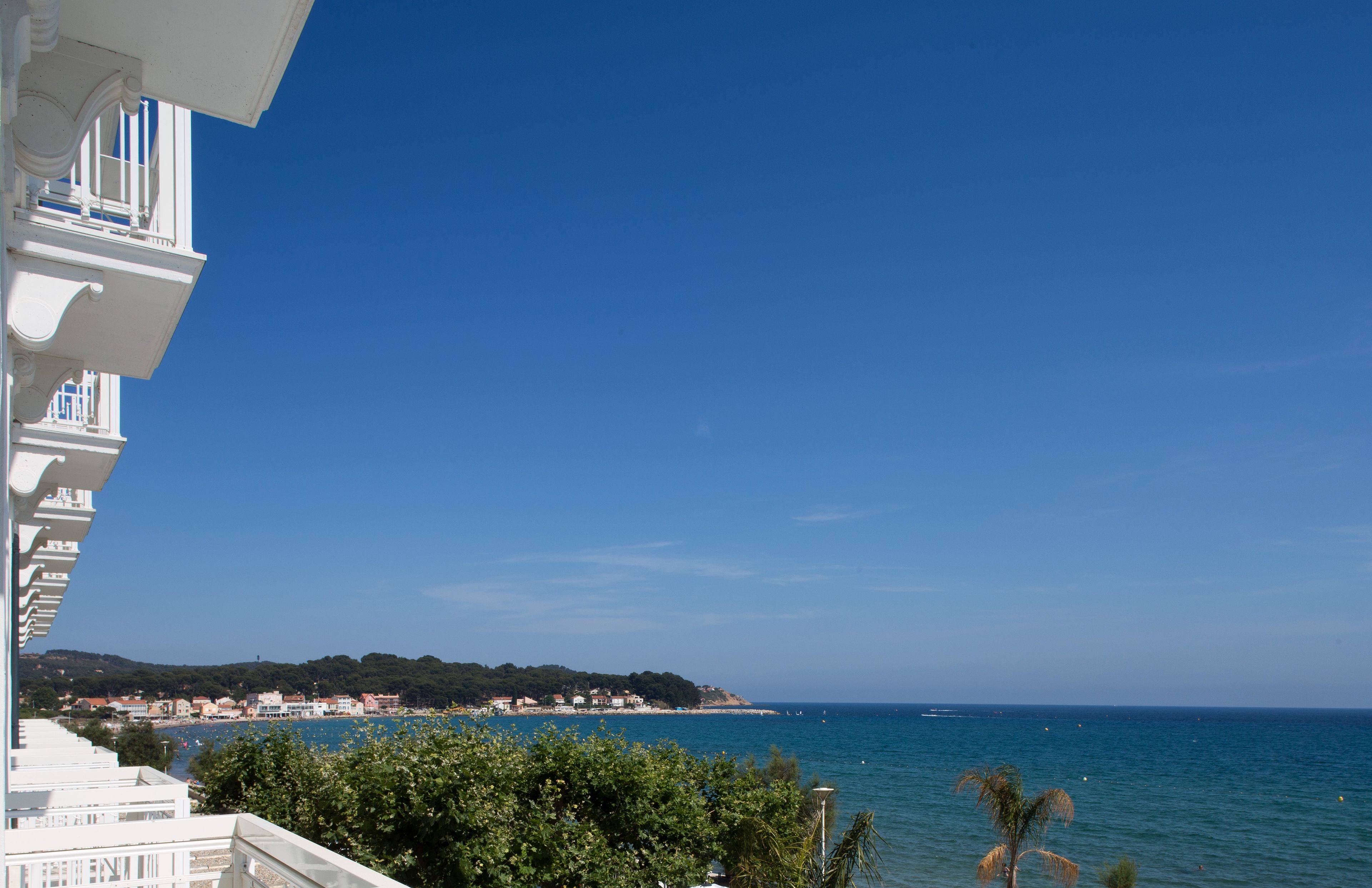 A coastal view with a balcony overlooking the sea, a clear sky, and a distant shoreline with buildings.