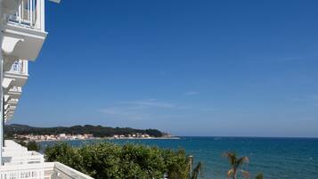 A coastal view with a balcony overlooking the sea, a clear sky, and a distant shoreline with buildings.