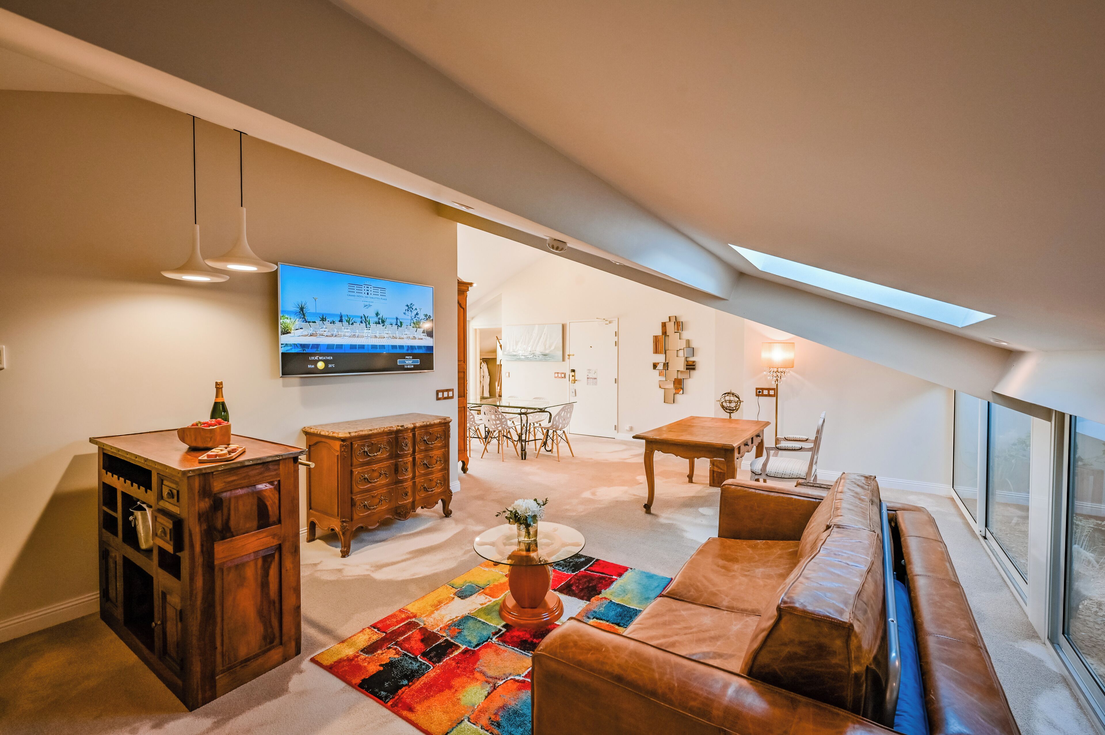 Un espacio habitable estilo loft con techo alto, un televisor de pantalla plana, una mesa de comedor con sillas, un sofá, un mueble de madera y una alfombra colorida.