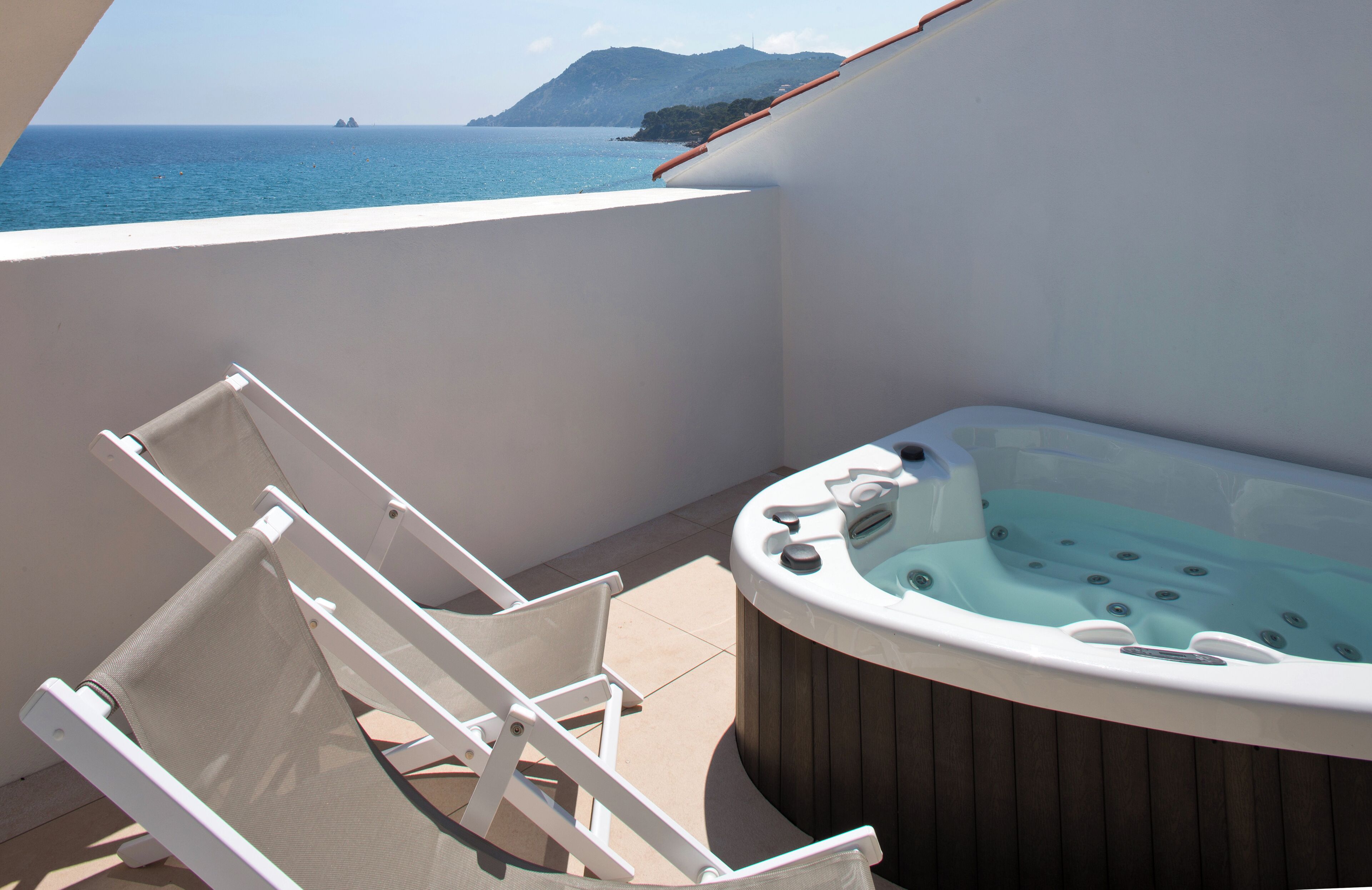 A balcony with a hot tub, a white chair, and a view of the sea.