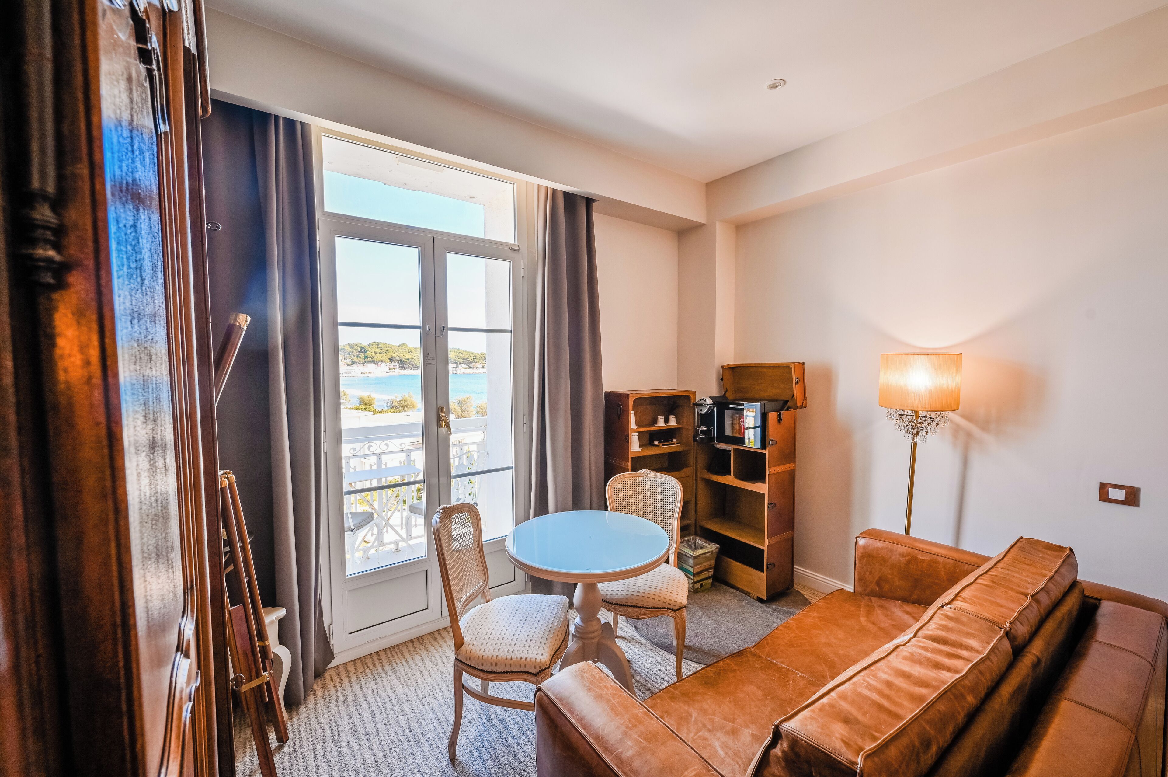 A room with a brown leather sofa, a round table, two chairs, a bookshelf, and a lamp.