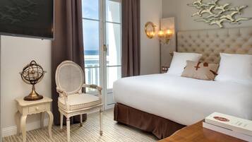 Une chambre d’hôtel avec un grand lit, une chaise, un téléviseur, un luminaire fixé au mur et une vue sur la mer.