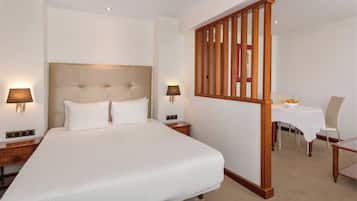 A hotel room with a large bed, two bedside tables, a nightstand, a wooden partition, a small table with a chair, and a lamp.