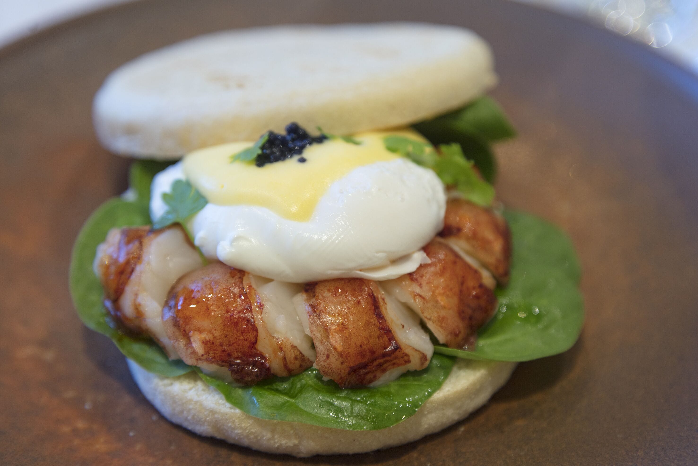 A sandwich with a poached egg, greens, and a sauce on a bun.