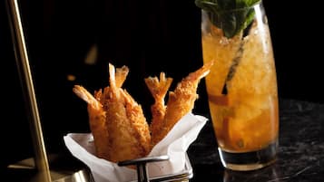 A tray with fried shrimp, a glass of iced drink with a straw, and a slice of orange on a dark surface.