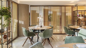 A modern dining area with round tables, green upholstered chairs, and a decorative bamboo screen. - Melia White House Apartments (London)