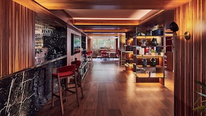 A modern kitchen with wooden paneling, a marble countertop, and red bar stools. - Melia White House Apartments (London)