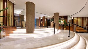 A spacious lobby with large columns, a curved staircase, and a reception area. - Melia White House Apartments (London)