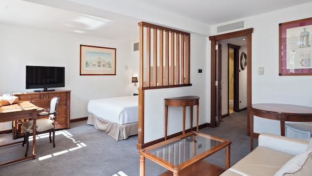A hotel room with a bed, desk, chair, TV, and a glass coffee table. - Melia White House Apartments (London)