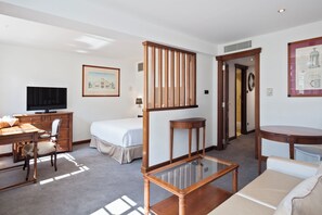 Een hotelkamer met een bed, bureau, stoel, televisie en een glazen salontafel.