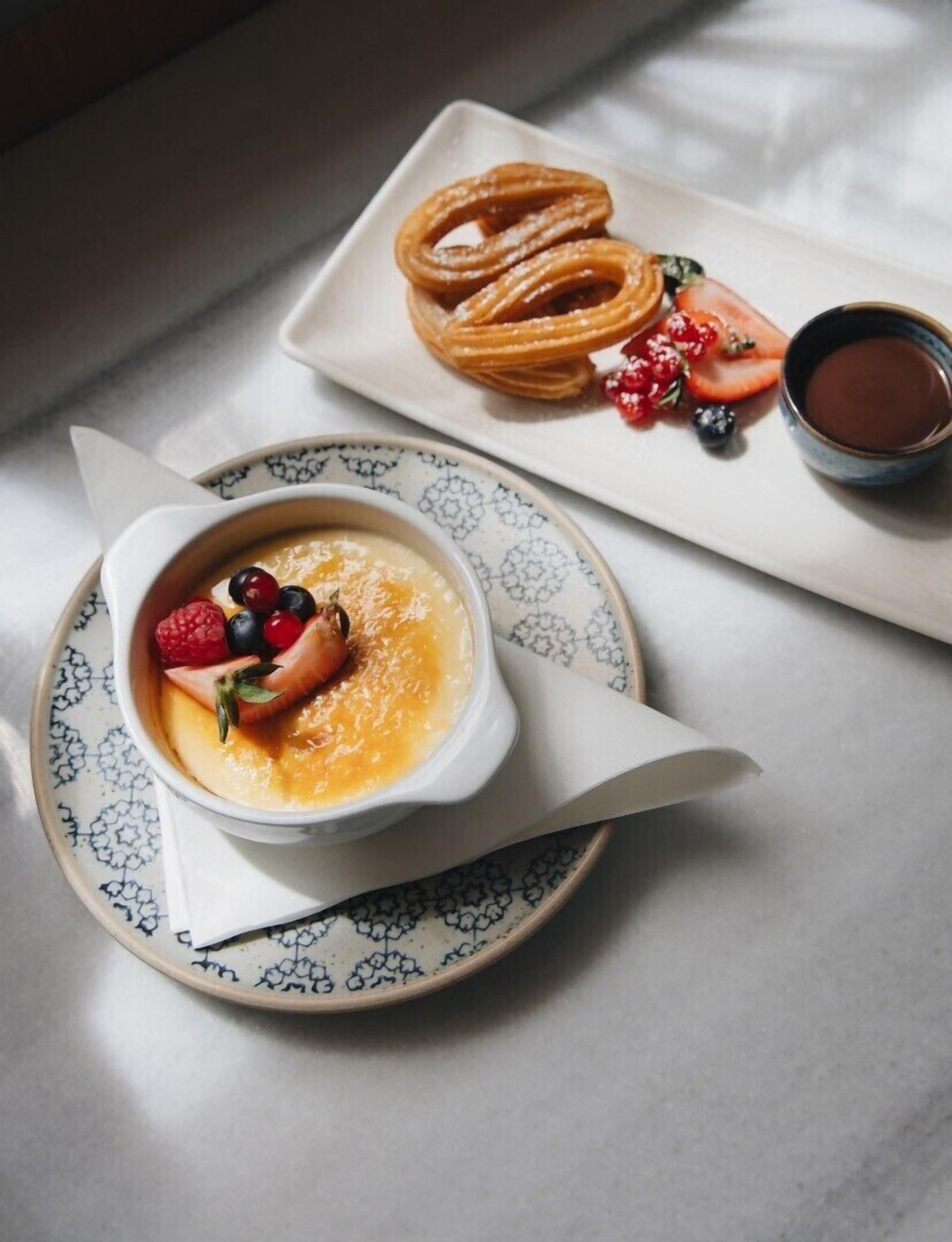 Une assiette de dessert avec un ramequin de crème brûlée, une assiette de churros et une tasse de sauce au chocolat.