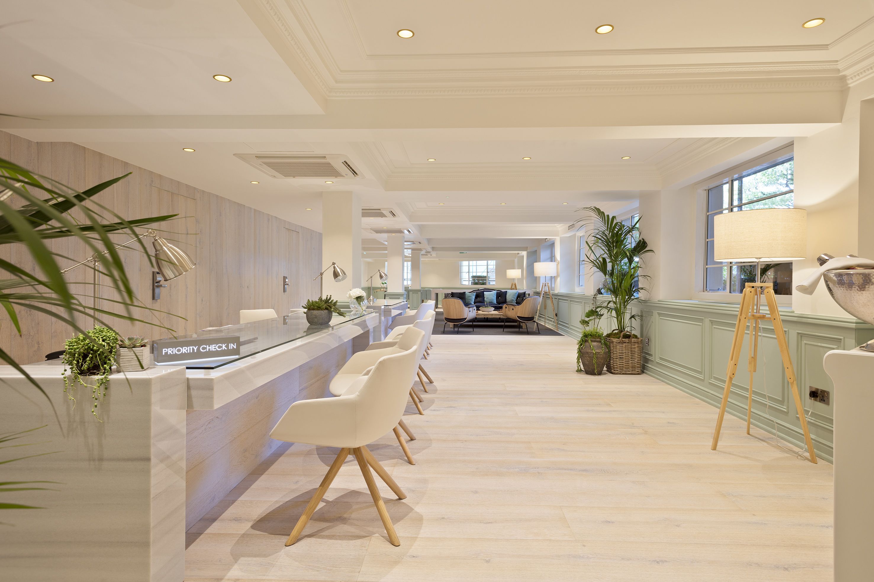 A spacious reception area with a priority check-in desk, multiple seating options, and potted plants.