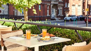 A table with breakfast items, including toast, eggs, and a glass of orange juice, set outdoors with a view of a city street and buildings in the background. - Melia White House Apartments (London)