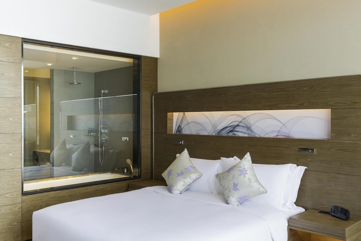 A modern hotel room with a large mirror, a bed with white linens, and a nightstand with a phone and a small table.