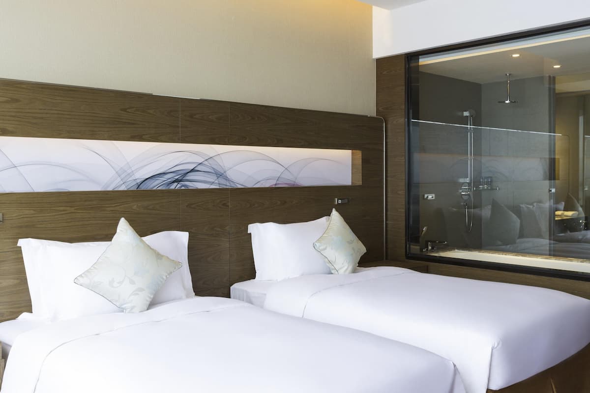A hotel room with two beds, a large window, and a wooden headboard.